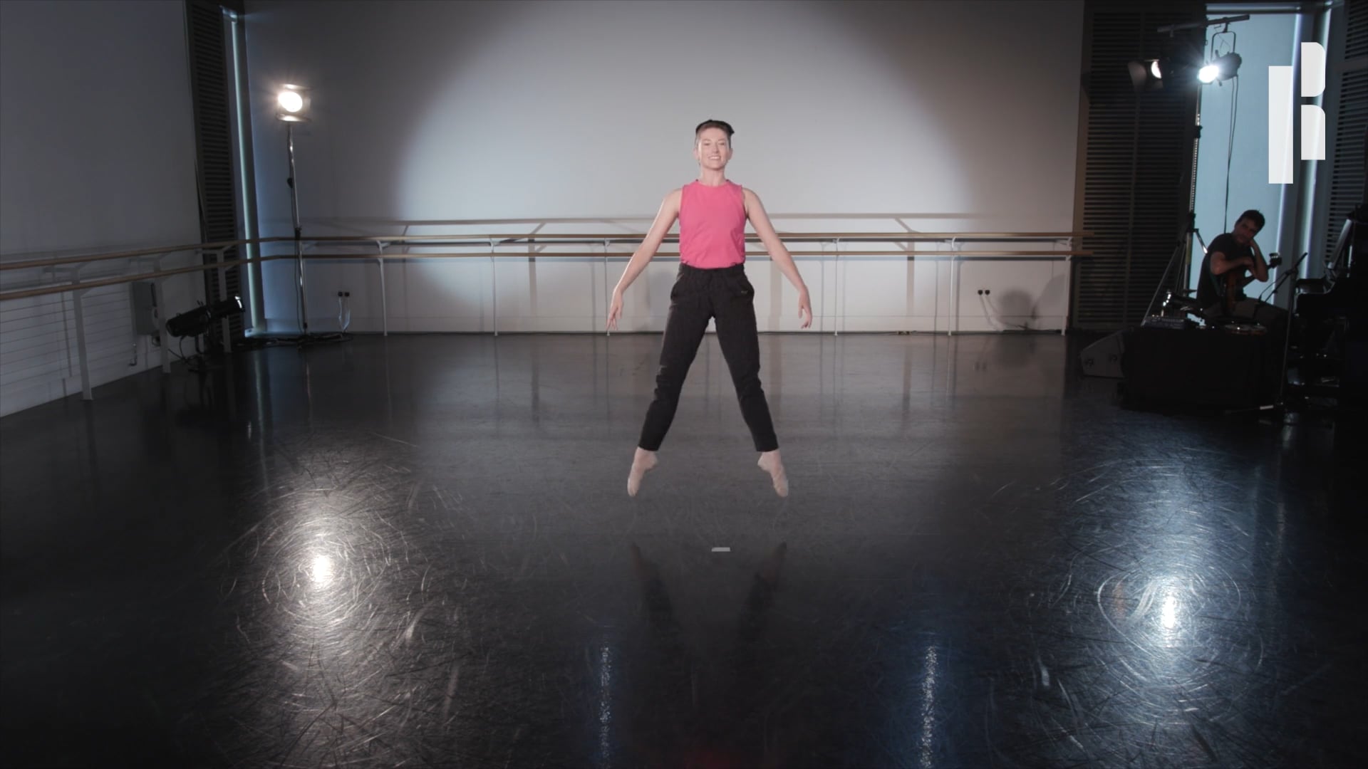 A man in a pink shirt is jumping in a dance studio.