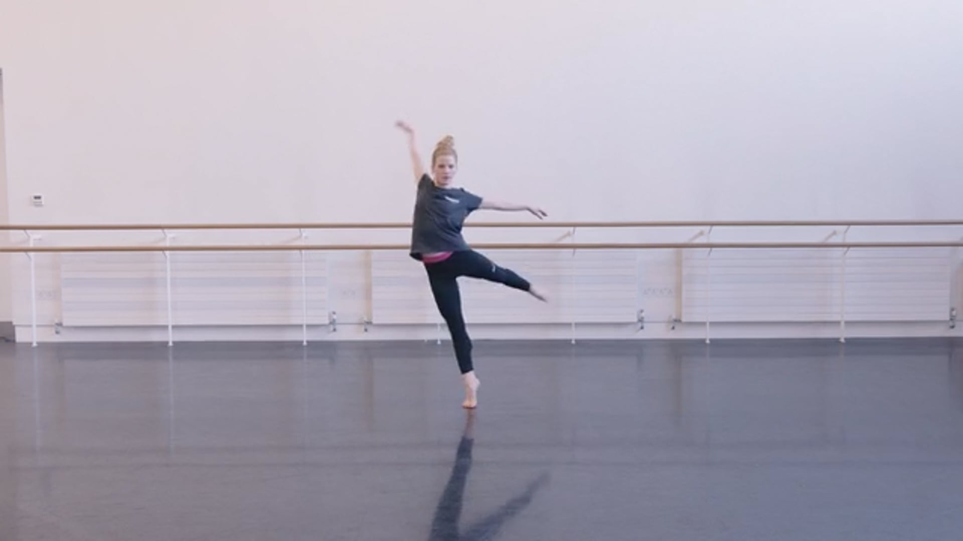 A woman in a black top and black leggings is dancing in a dance studio.