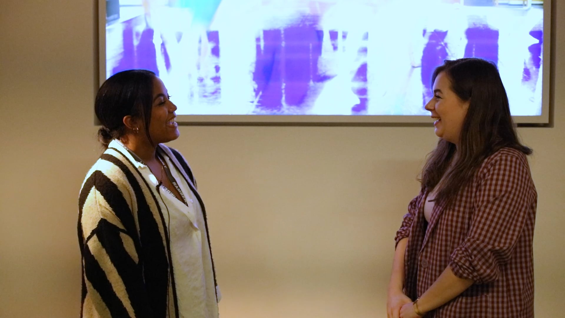Two women talking in front of a large screen.