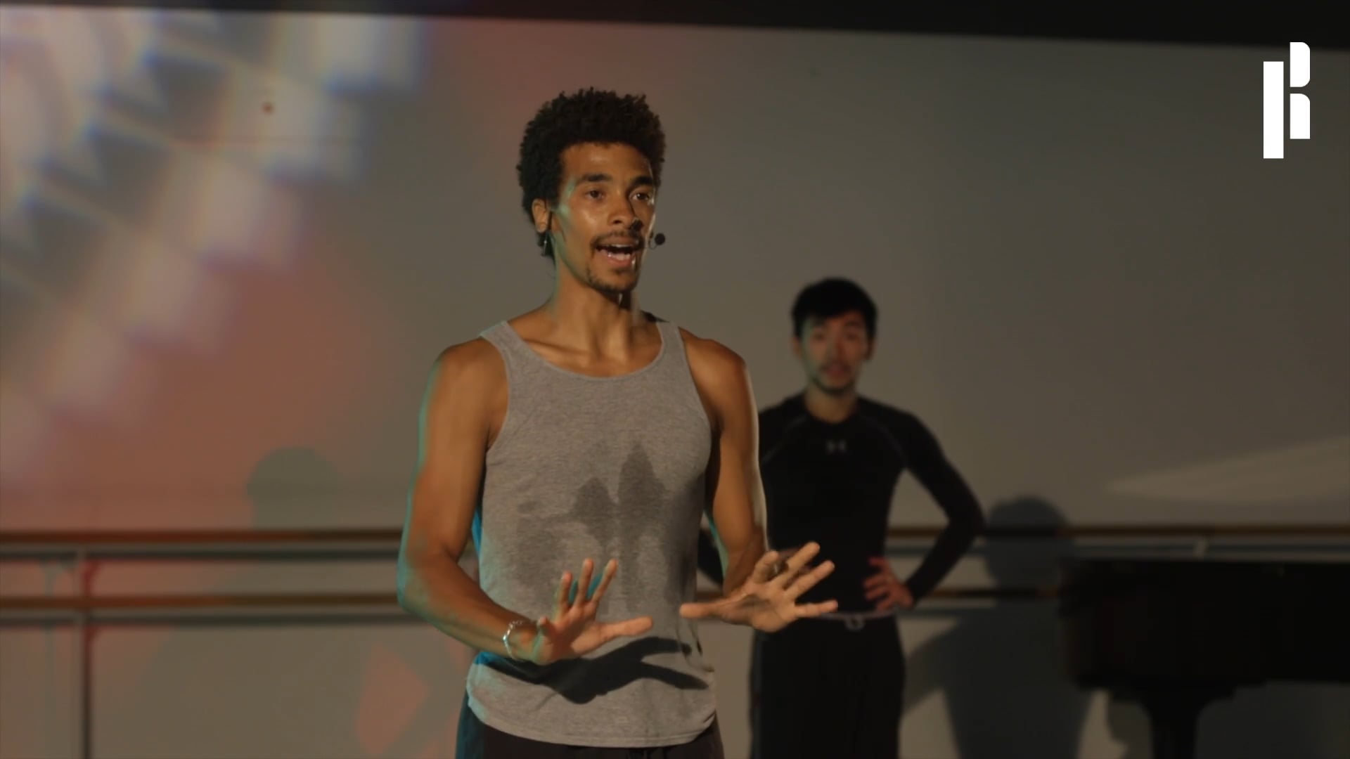A man in a tank top is standing in front of a piano.