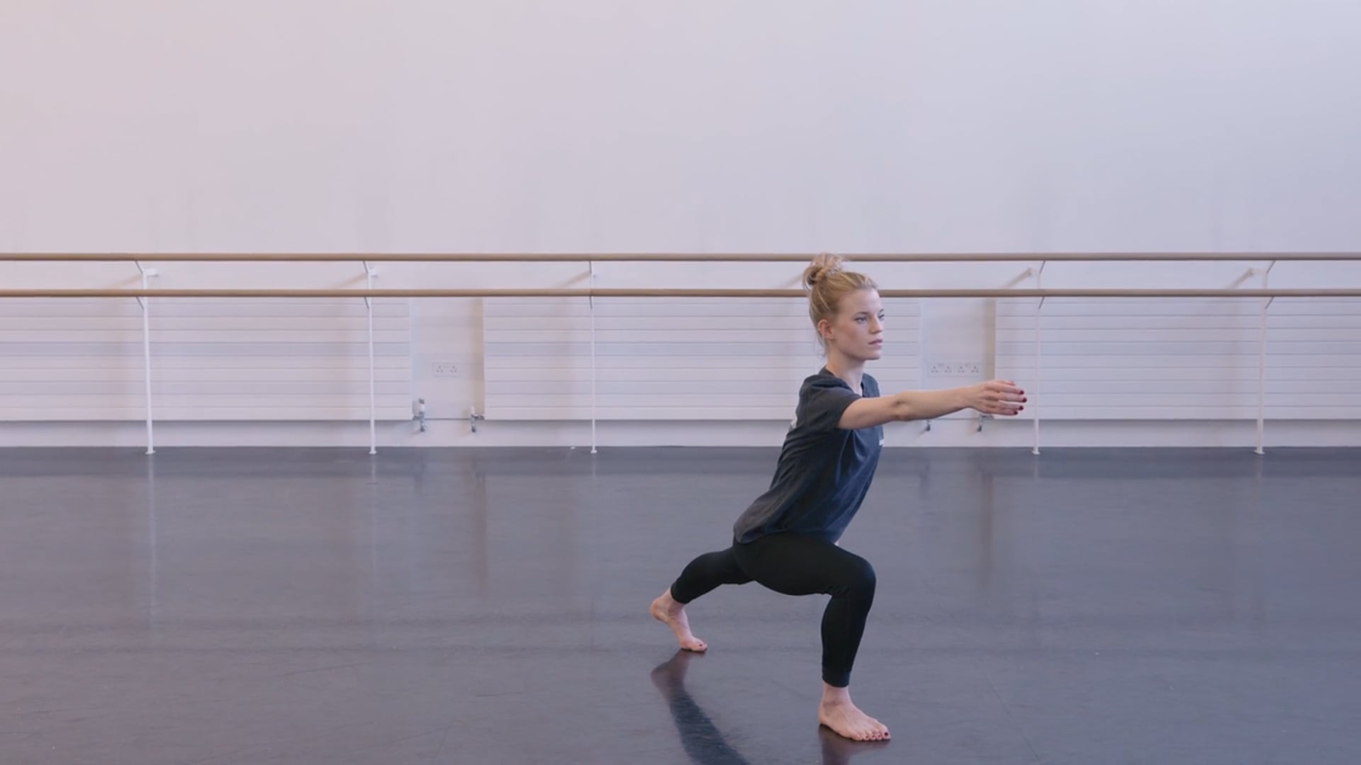 A woman in a black dress is stretching in a dance studio.