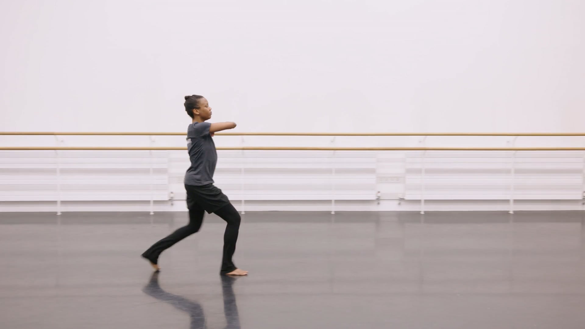 A man in a gray shirt is dancing in a dance studio.