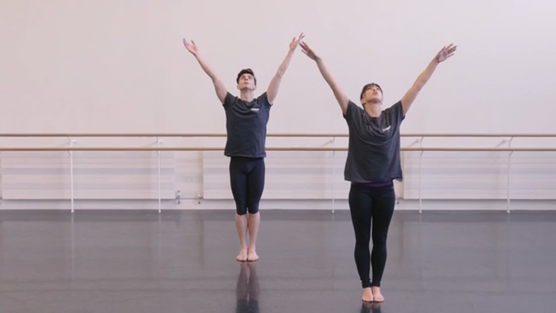 Two dancers with their arms raised in the air in a dance studio.