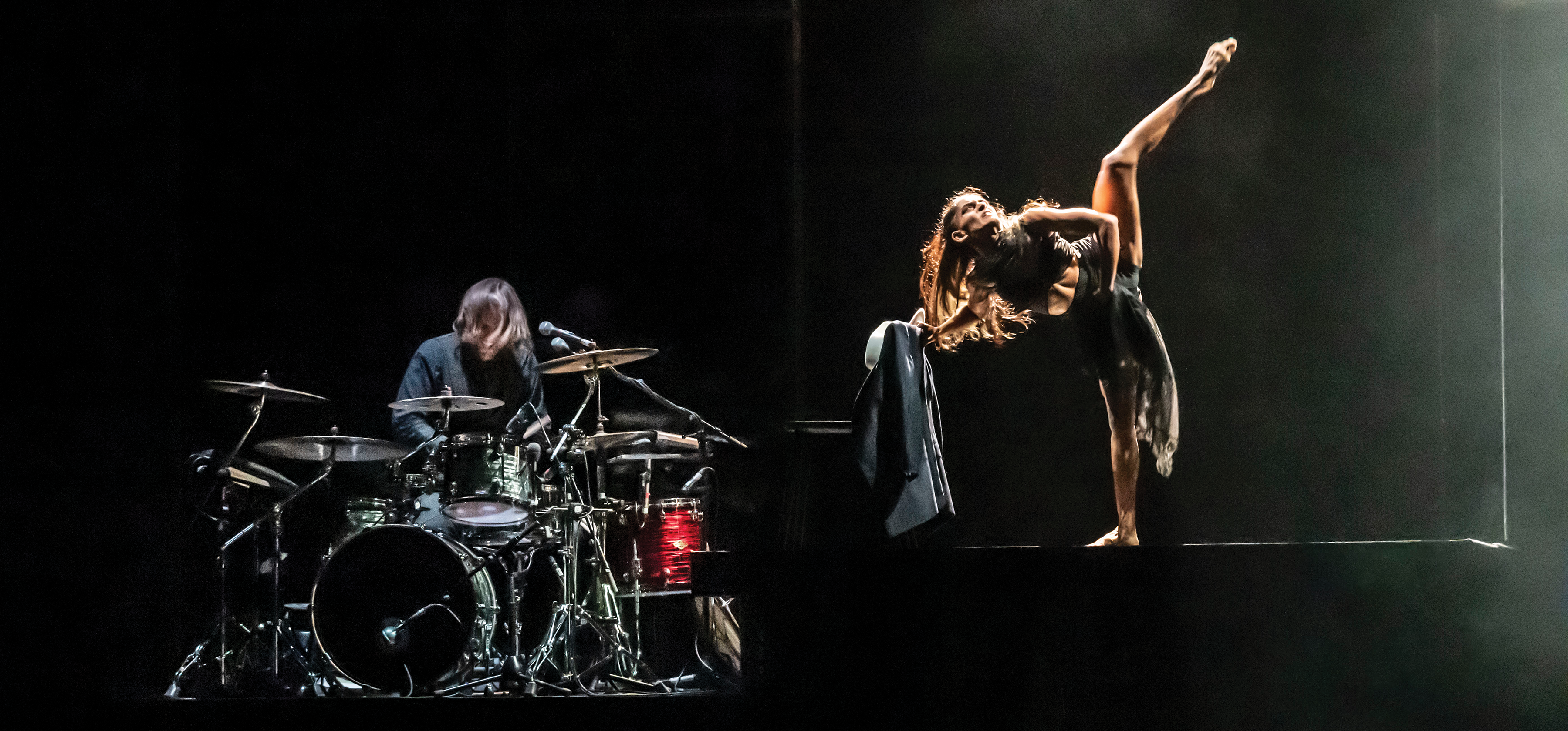 A drummer with a drum kit and a dancer kicking on stage