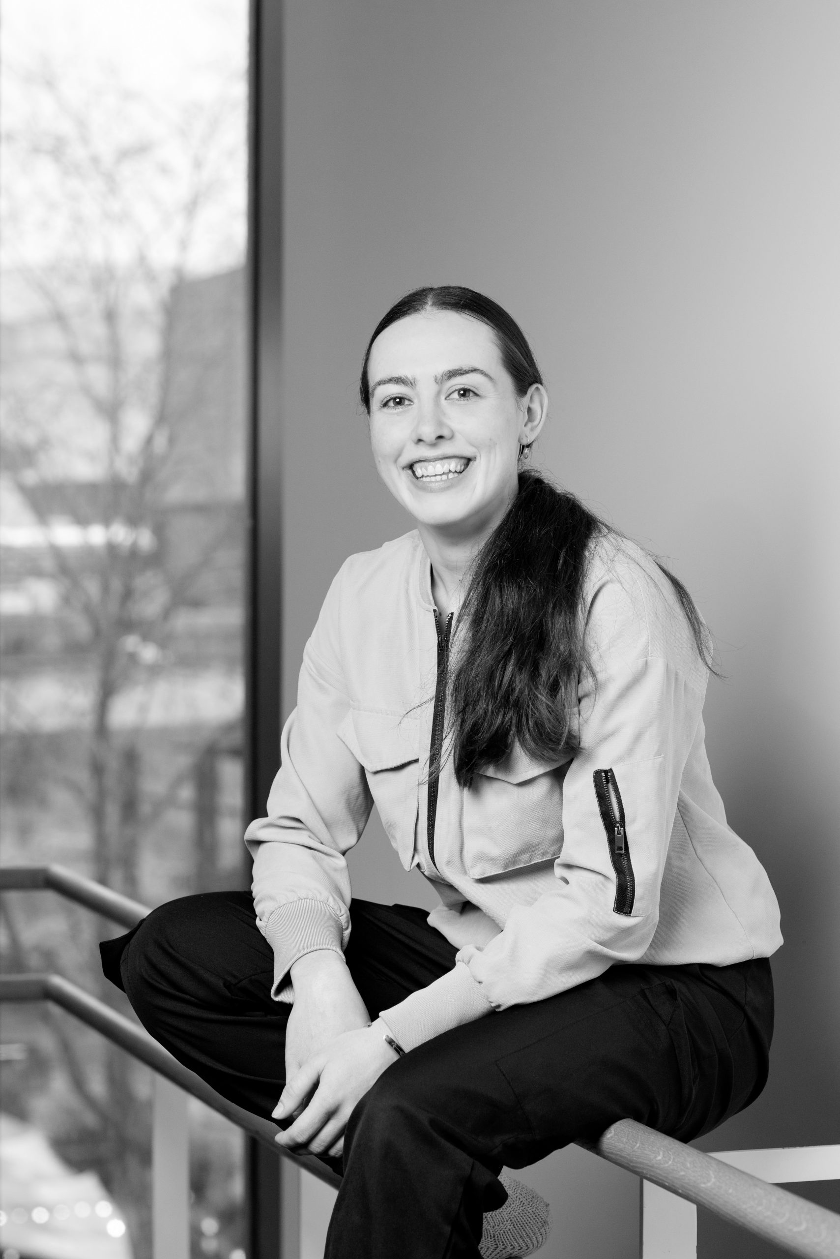 a black and white photo of a woman sitting on a railing.