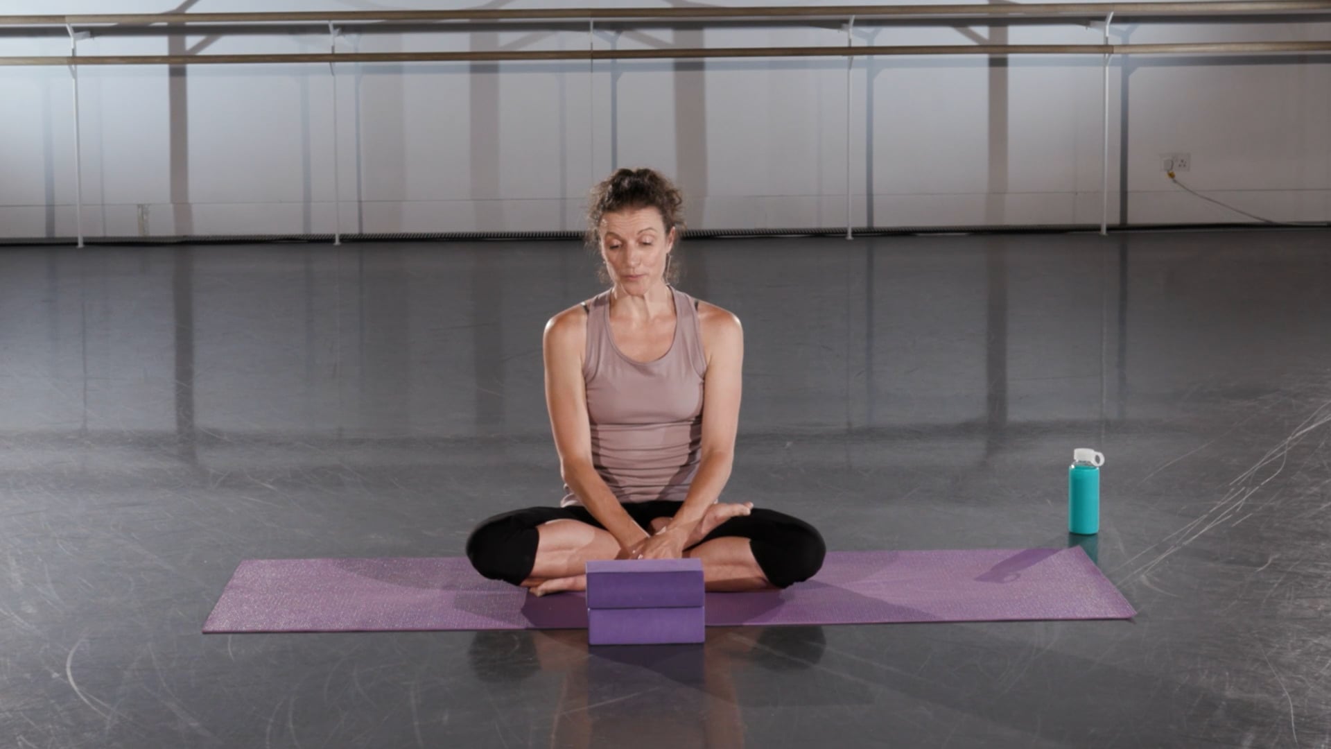 a woman sitting on a yoga mat in a gym.