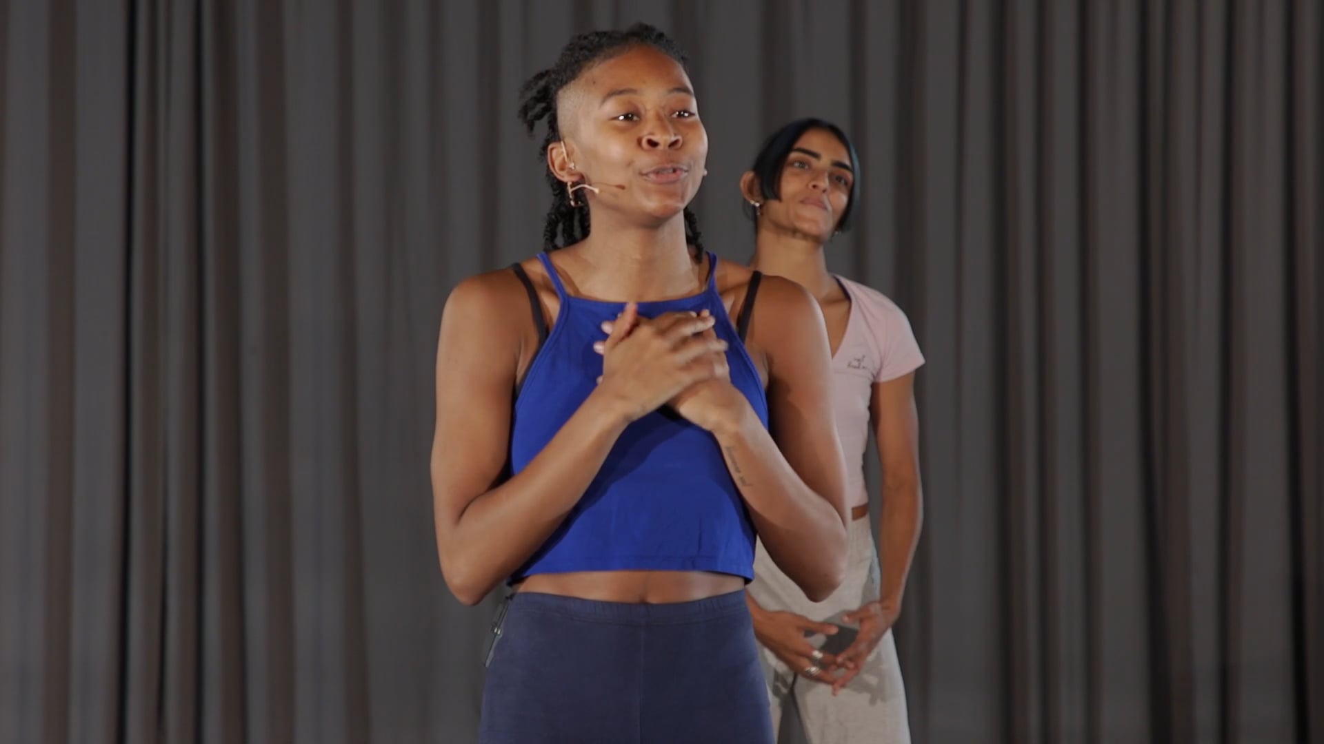 two women standing next to each other in front of a curtain.