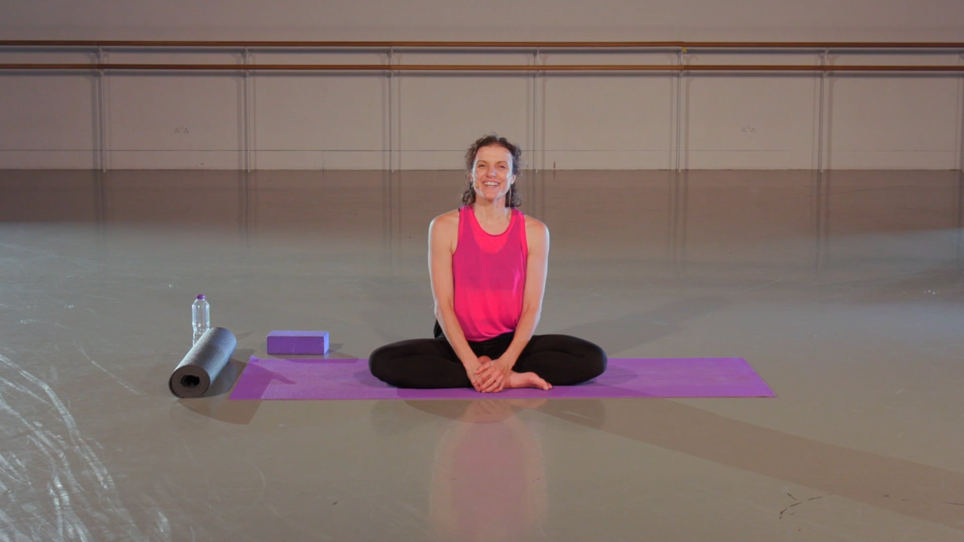 a woman sitting on a yoga mat in a gym.