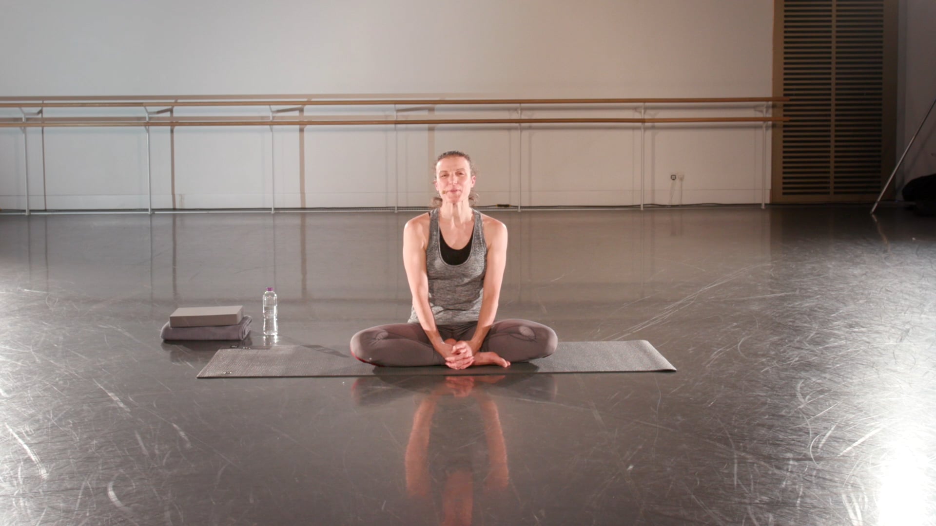 a woman sitting on a yoga mat in a gym.
