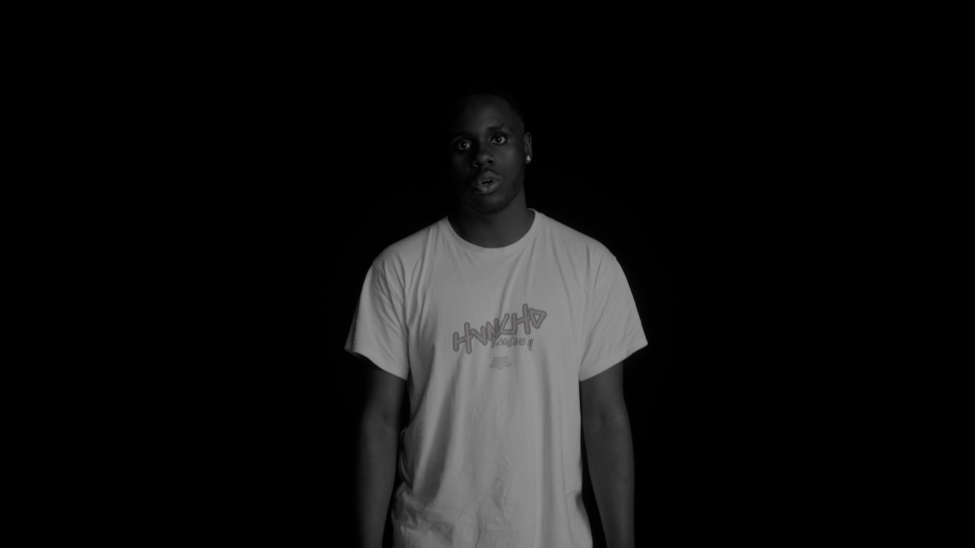 a man standing in the dark with his hands in his pockets.