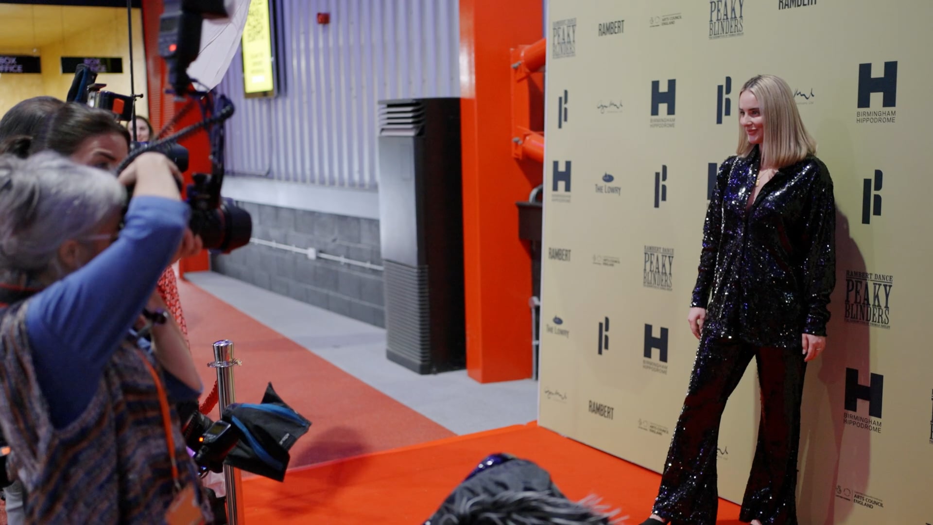 a woman standing in front of a camera on a red carpet.