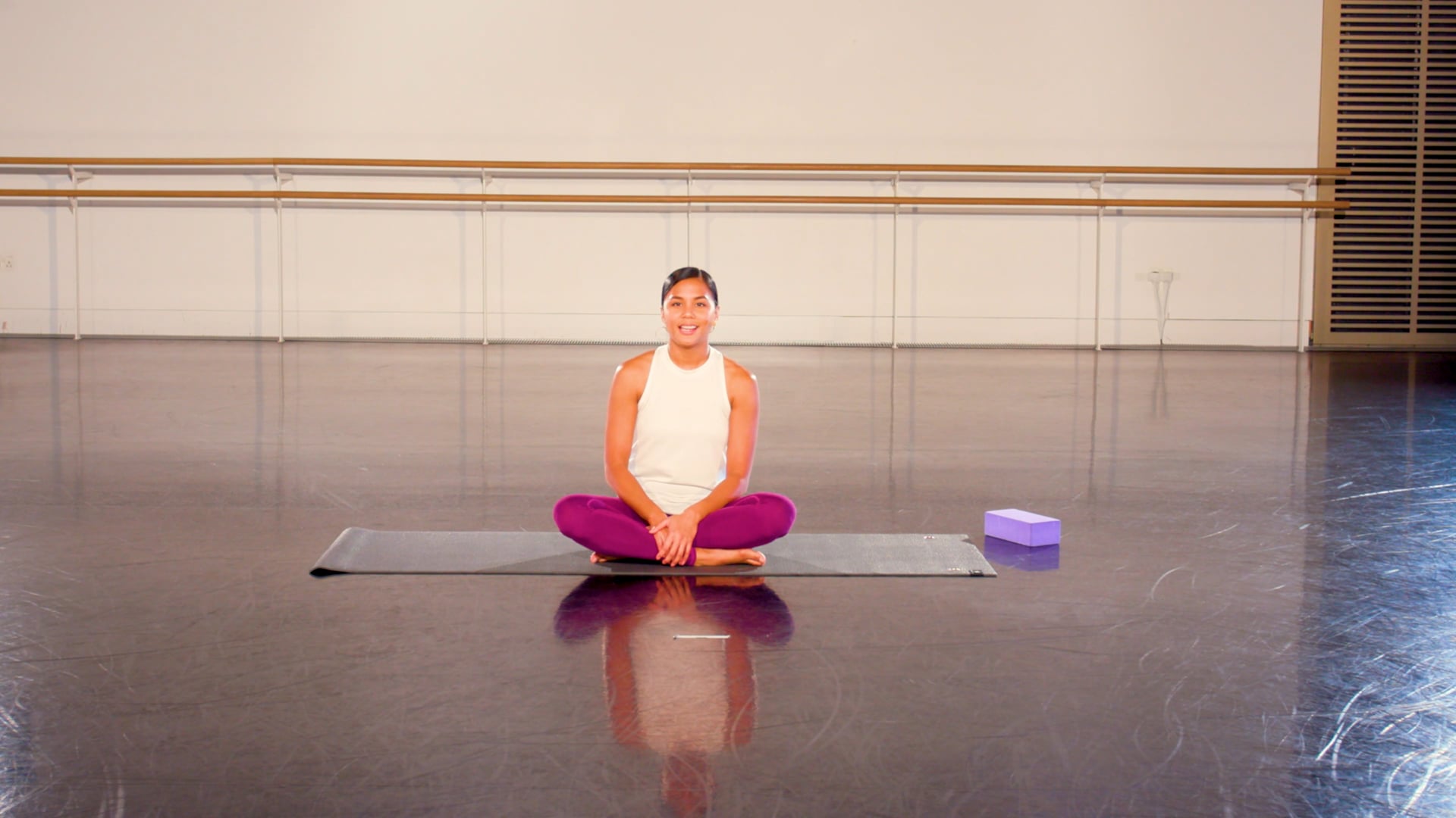 a woman sitting on a yoga mat in a gym.