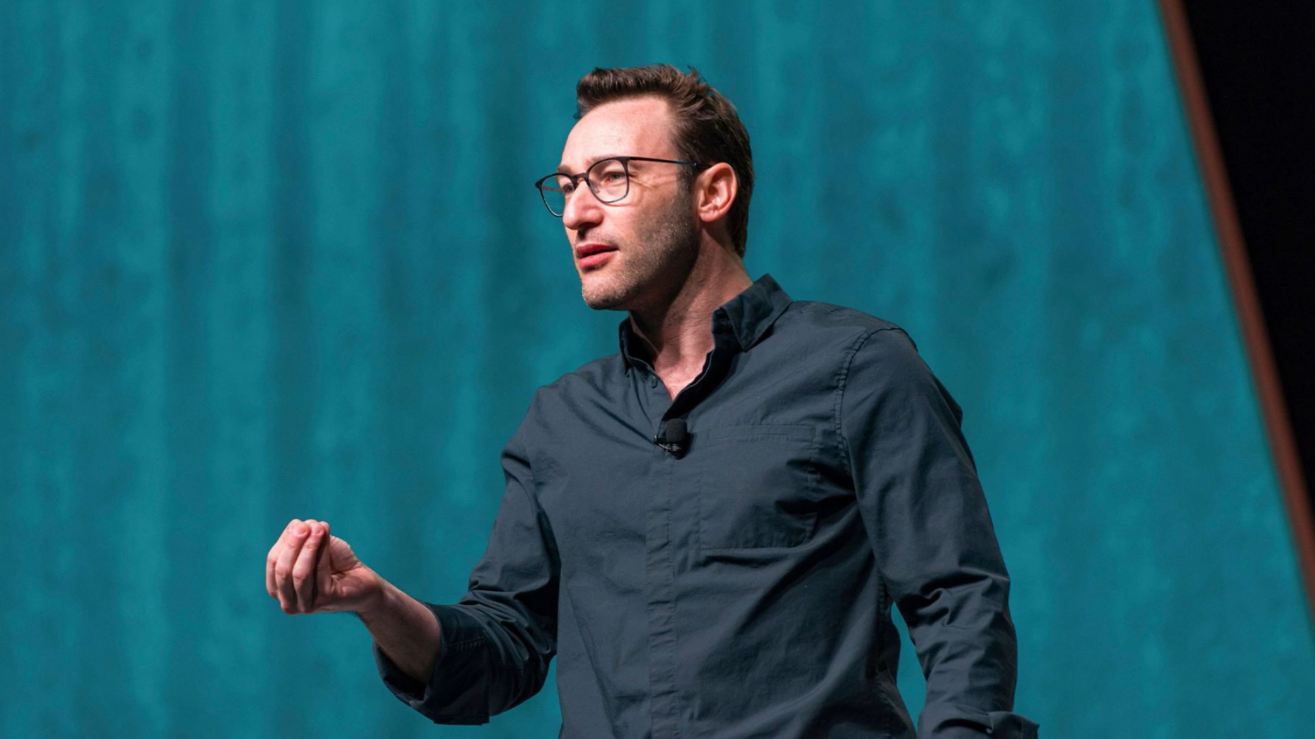 a man in a black shirt and glasses standing in front of a blue wall.