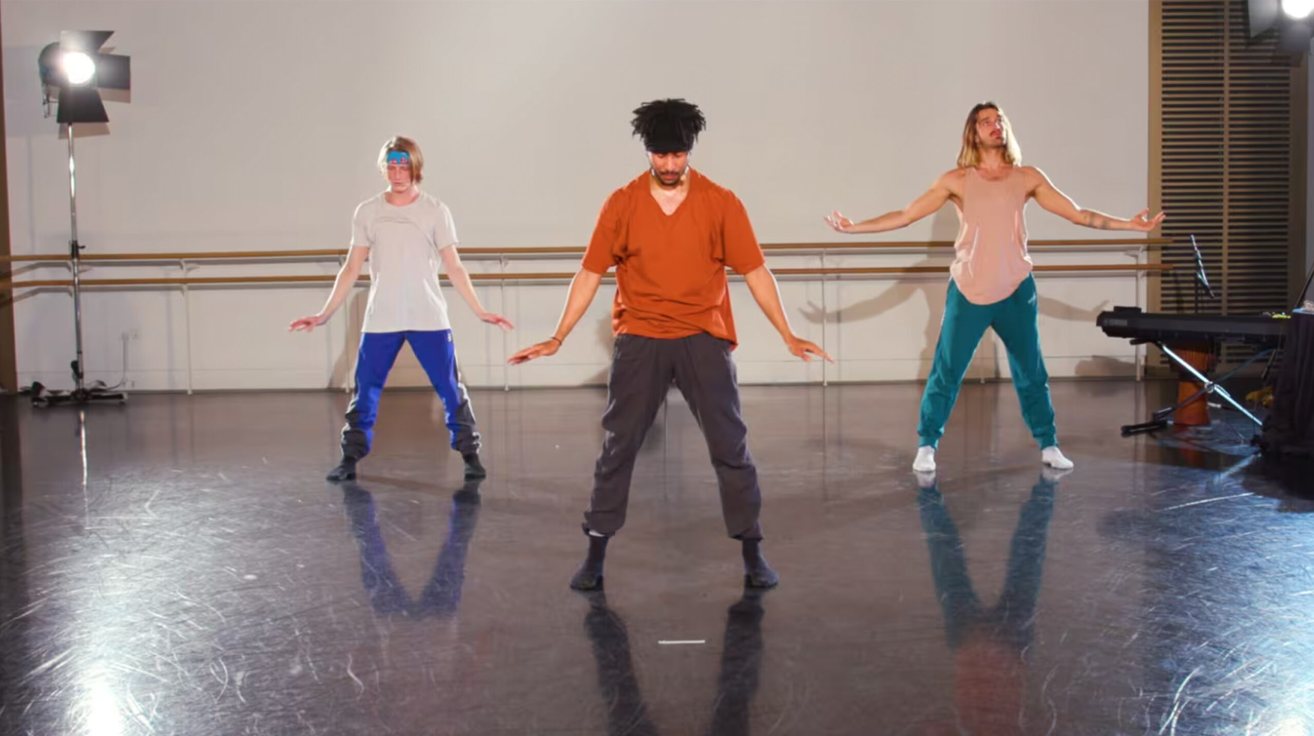 Teacher wearing an orange shirt and with his students behind him inside Rambert's studio