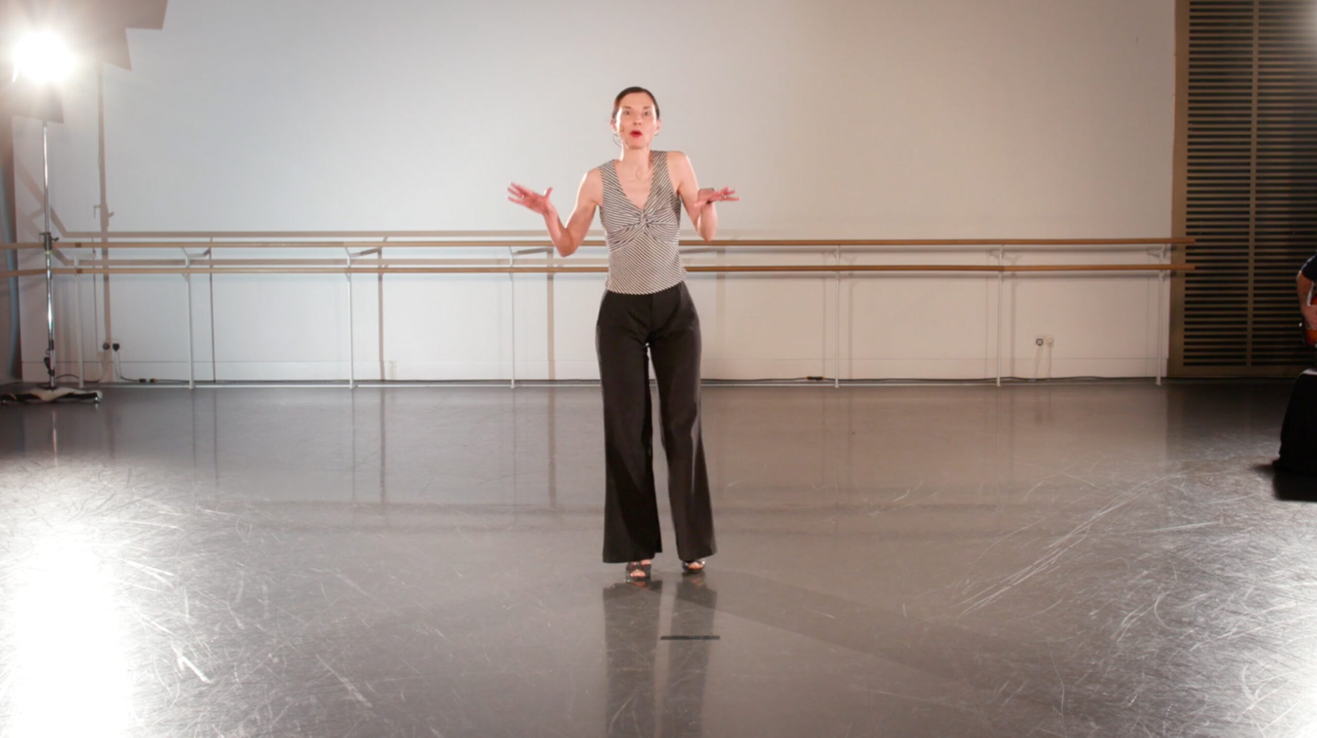White woman with a grey shirt and black trousers inside a dance studio to teach a Disco Class to people over 60 years-old