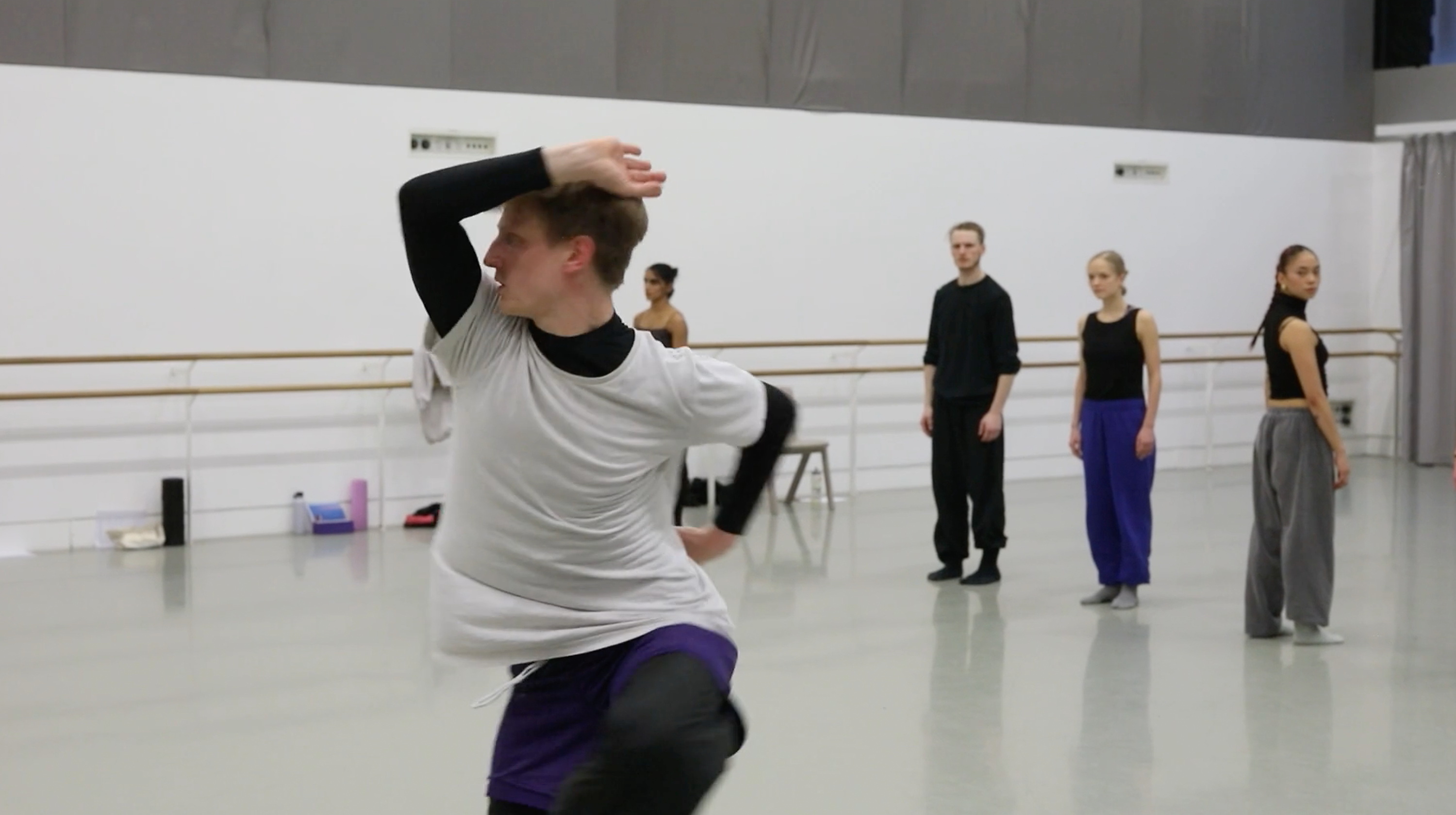Rambert dancer, a man with a white t-shirt and black trousers, flipping his body during a rehearsal in studio