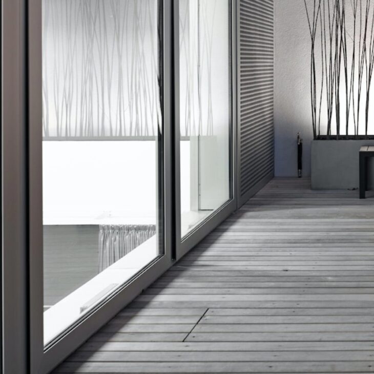 A modern, minimalist space with a wooden deck and large glass windows. The interior features light gray walls and two tables with chairs. 

.