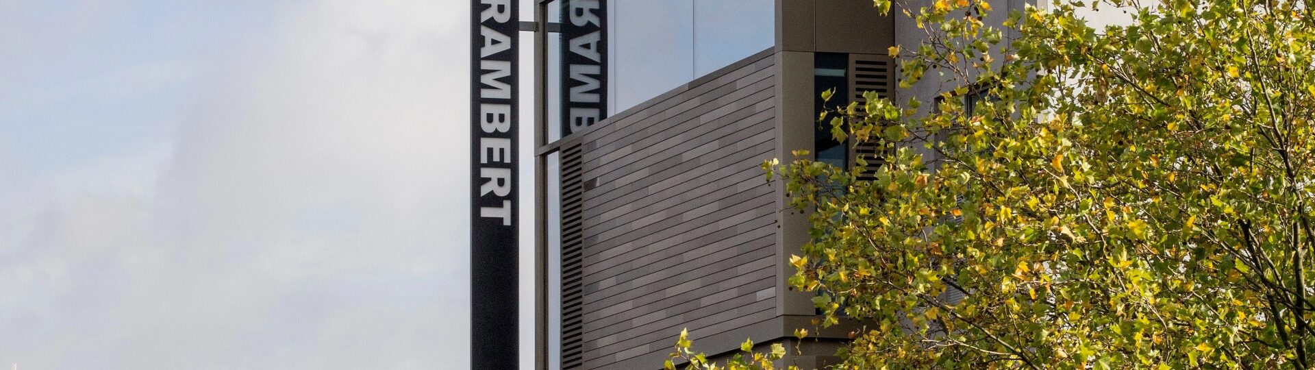 Modern building with the name "Rambert" displayed in large letters on the side, adjacent to a tree with green leaves.