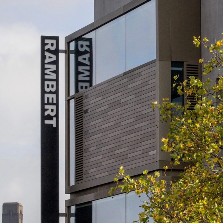 Modern building with the name "Rambert" displayed in large letters on the side, adjacent to a tree with green leaves.