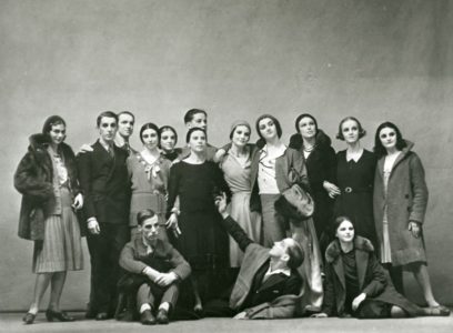 Black and white photo of a group of men and women posing together. Two men are sitting on the floor in front, with the others standing closely behind them.