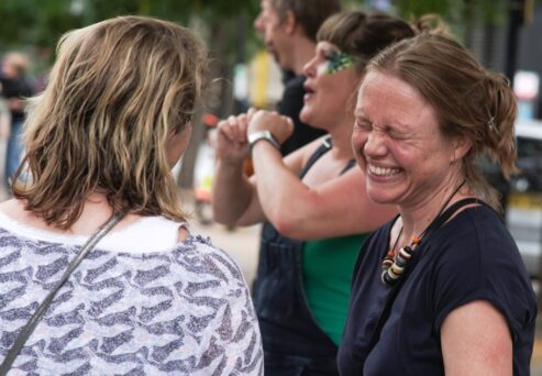 Four people are outdoors in a casual setting, with one woman smiling broadly and the others engaged in conversation.