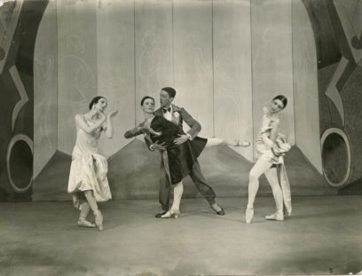 Four ballet dancers pose on a stage; two are standing close and performing a dance move, while the other two pose gracefully on either side. The background features an abstract design.
