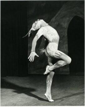 A dancer in a bird-like costume performs on stage with one leg lifted and arms gracefully extended.